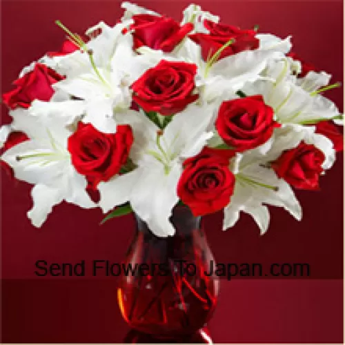 Roses rouges et lis blancs avec quelques fougères dans un vase en verre