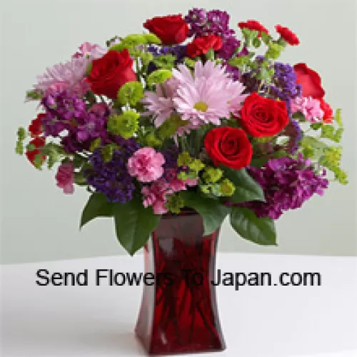 الورود الحمراء، والقرنفل الوردي وزهور موسمية متنوعة أخرى في وعاء زجاجي