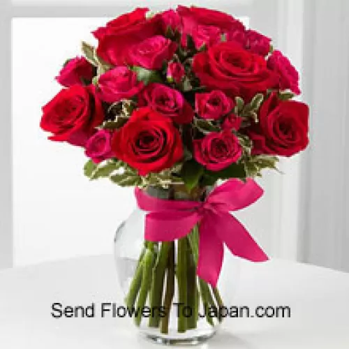 19 rote Rosen mit saisonalem Füllmaterial in einer Glasvase, dekoriert mit einer rosa Schleife